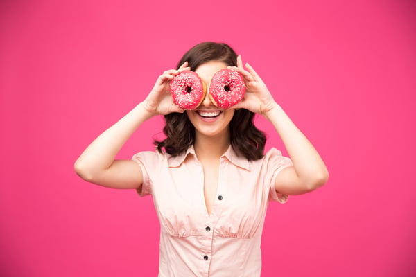 Woman covering her eyes with donut over pink donut